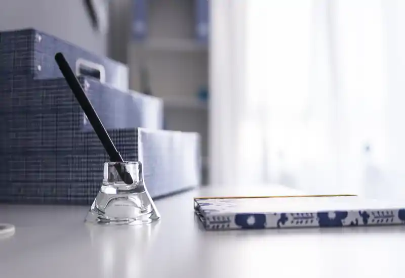 Un angolo scrivania luminoso e minimale con portapenne in vetro, scatole portaoggetti fantasia e un taccuino su una superficie illuminata — perfetto per un piccolo ufficio domestico.