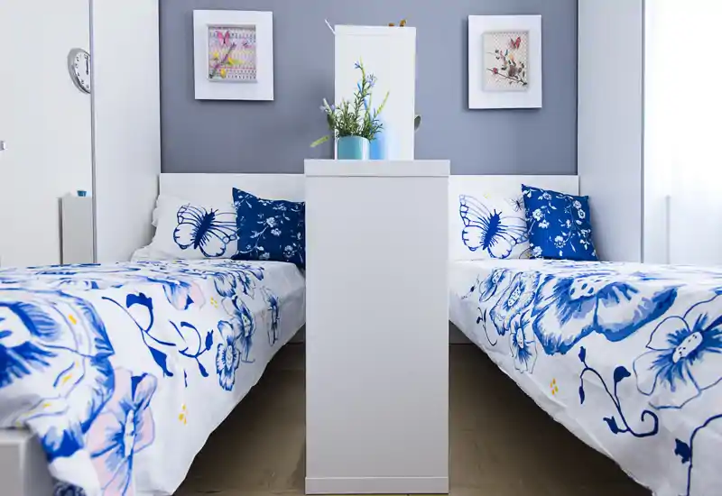 Symmetrical twin bedroom with bright blue floral bedding, decorative pillows and fresh accents; well lit and neatly styled for a welcoming stay.