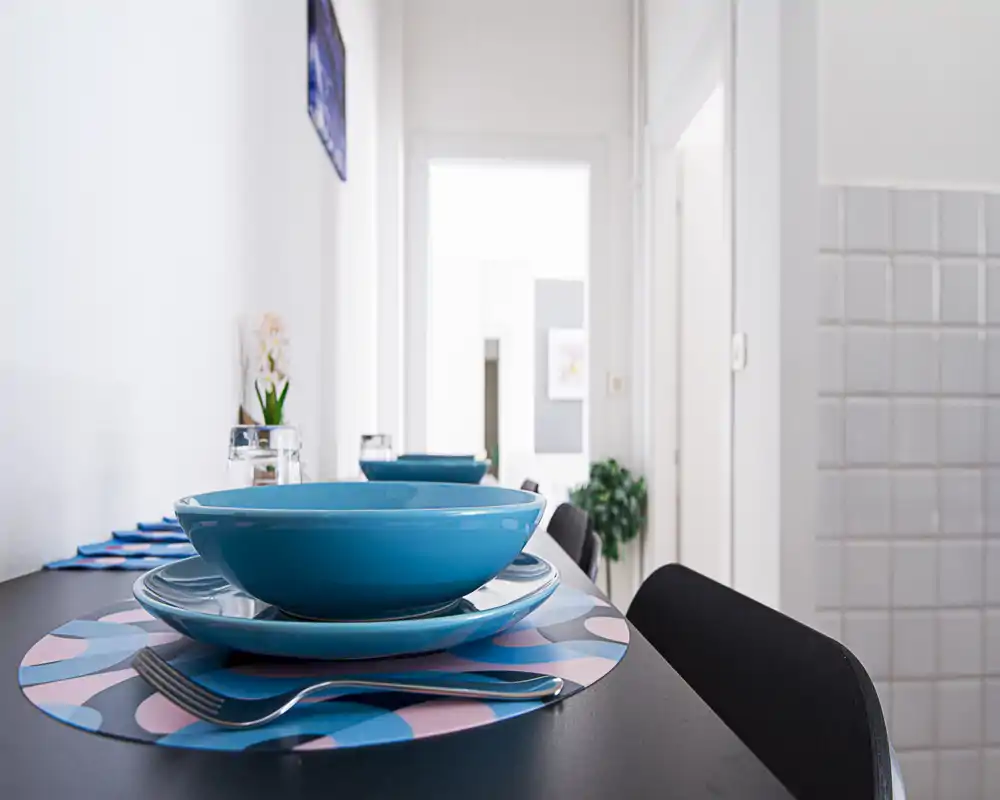 Primo piano di un tavolo apparecchiato con ciotole turchesi e tovagliette decorative; ambiente moderno e luminoso perfetto per mostrare la zona pranzo.