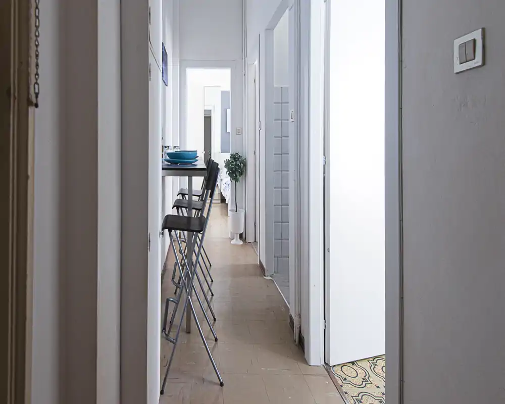 Corridoio d'ingresso stretto con un bancone alto e sgabelli pieghevoli, che conduce alle stanze interne. Pulito e minimale, adatto ad appartamenti compatti.