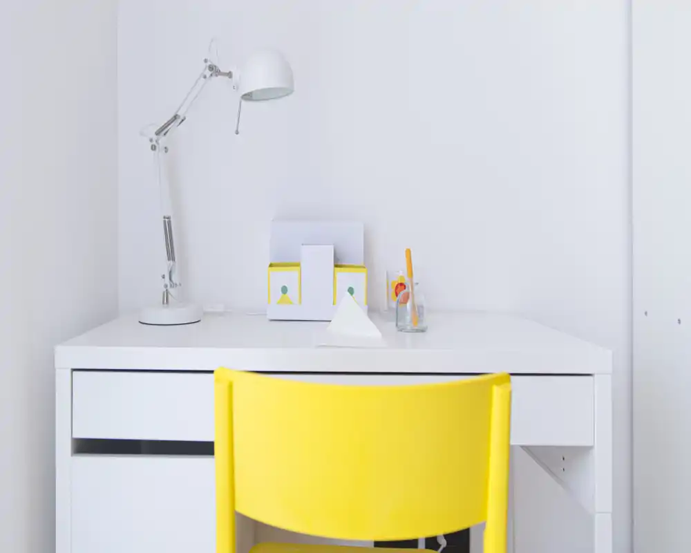 Espacio de trabajo minimalista y luminoso con escritorio blanco, lámpara ajustable y silla amarilla vibrante — ambiente limpio y moderno ideal para concentrarse.