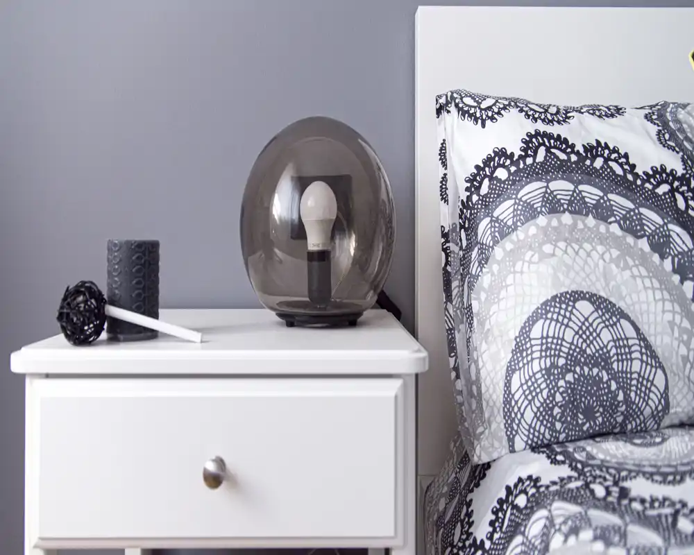 Close-up of a bedside table and the edge of a patterned bed with a decorative lamp and accessories, showing a neat, modern bedroom detail.