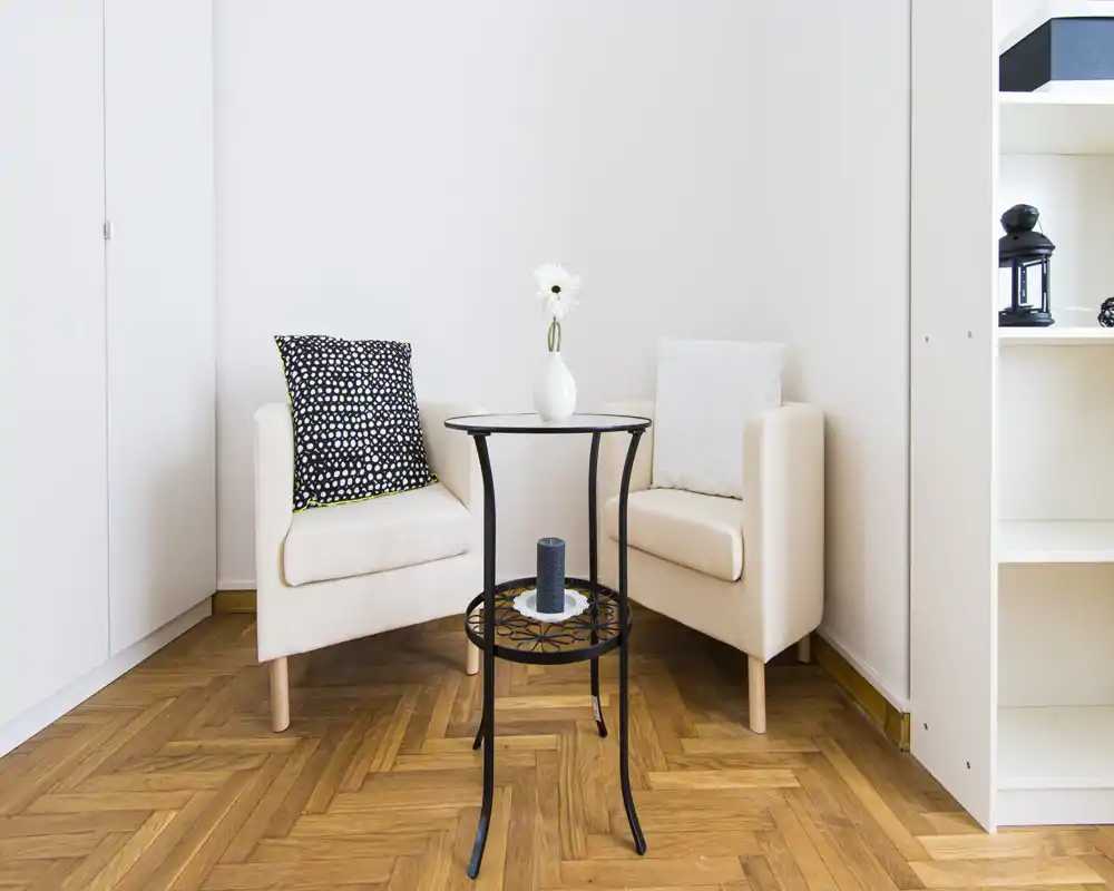 A bright, cozy living corner with two armchairs, a small decorative side table and tasteful accents, ideal for relaxing or conversation.