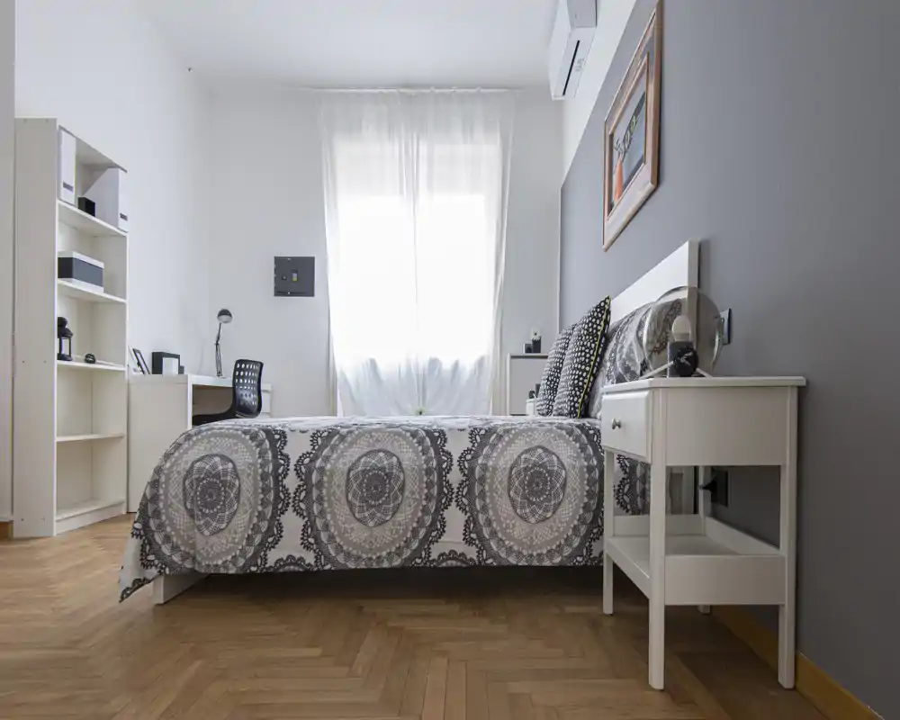 Bright, modern bedroom with a patterned double bed, bedside table and desk by the window. Clean lines, neutral tones and natural light create a calm, inviting space ideal for rental listings.