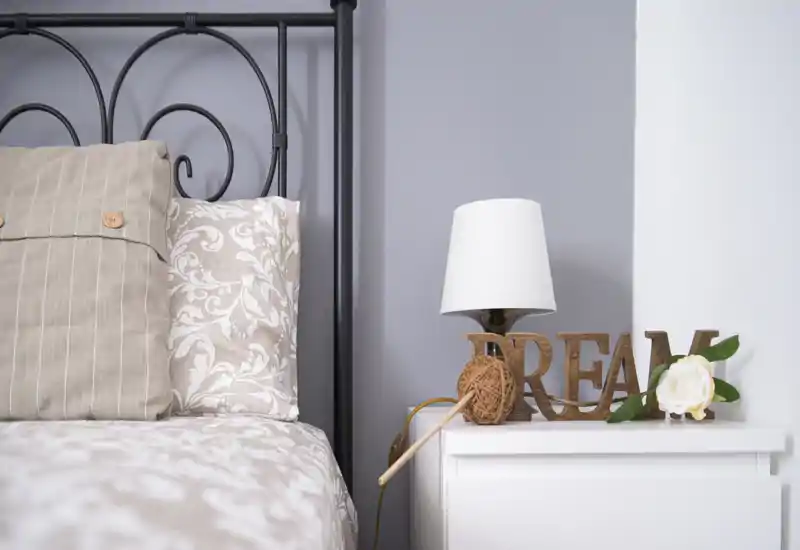 Cozy bedroom detail with a patterned duvet, decorative cushions and a styled bedside table featuring a lamp and floral accent — bright, well-composed shot ideal for listing photos.