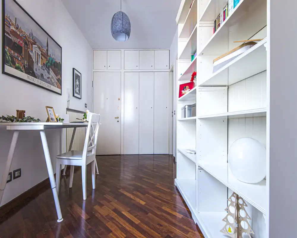Bright entry hallway with built-in closets, polished wood floor, a white desk and shelving — tidy and well lit, suitable as an entry or small home office area.