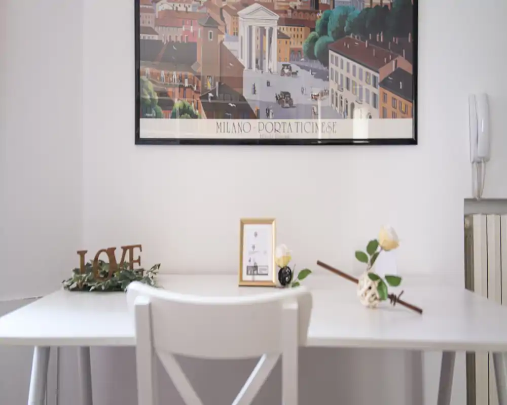 Bright, styled dining/desk area with a white table, decorative flowers and a framed print — a cozy spot for meals or work.