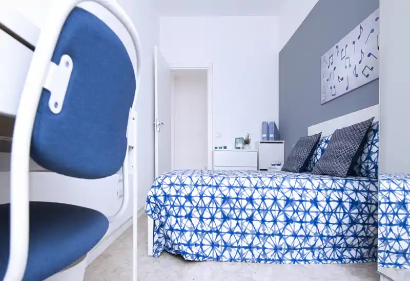 Bright, modern bedroom with a blue geometric bedspread and matching cushions. The room features a small white nightstand, simple wall art and a tidy minimalist décor ideal for short-term rentals.