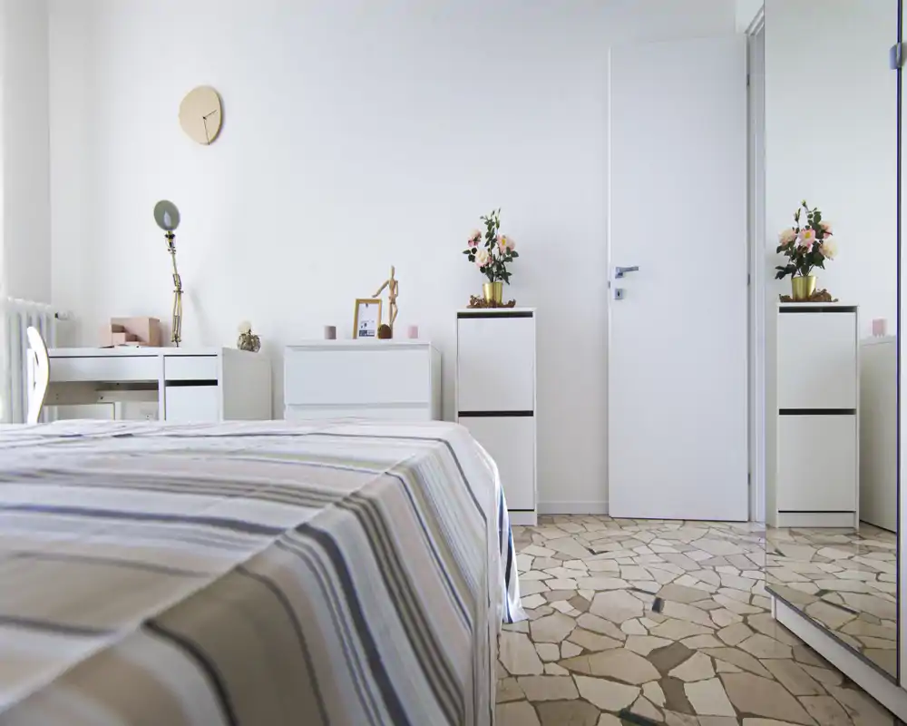 Chambre lumineuse et minimaliste avec une couette rayée, des rangements blancs et des fleurs décoratives ; bien éclairée et soignée pour des annonces.