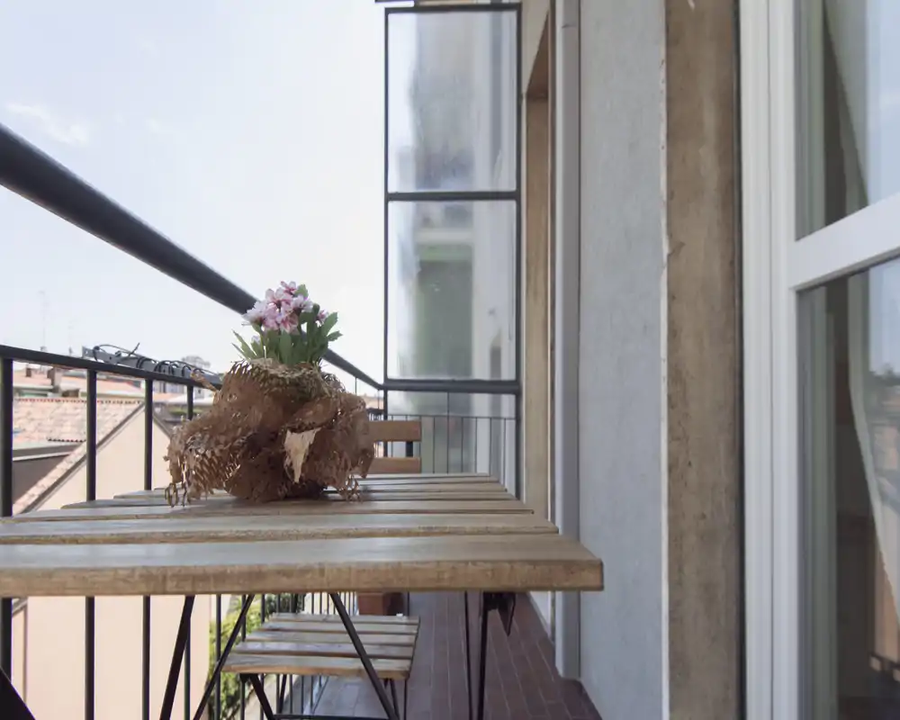 Balcon étroit et ensoleillé avec table en bois et chaises pliantes, décoré d'une petite plante en pot—idéal pour un café matinal avec vue sur la ville.