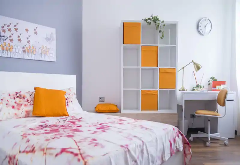 Camera da letto moderna e luminosa con biancheria floreale, cuscini arancioni e una scrivania ordinata con scaffalatura — perfetta per soggiorni confortevoli e smart working.