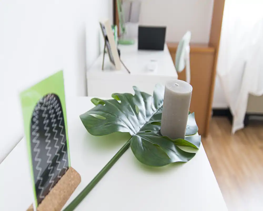 Close-up of a dresser surface with decorative leaf and candle in a bright, softly lit bedroom corner.