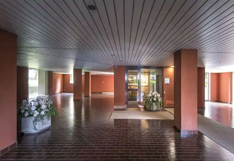 Ampio ingresso condominiale con pavimento in piastrelle, colonne e composizioni floreali decorative — area d'ingresso luminosa e simmetrica ideale per mettere in risalto gli spazi comuni.