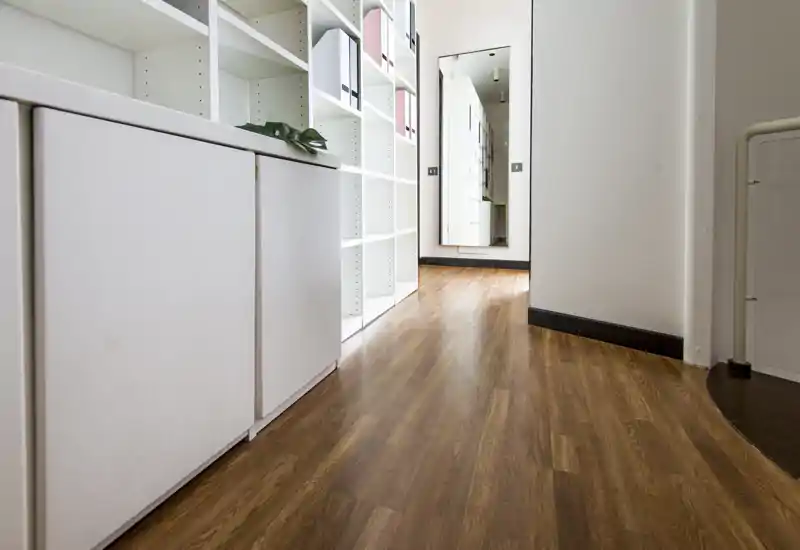 Ingresso/corridoio luminoso con pavimento effetto legno, armadietti integrati e scaffalatura a vista; un grande specchio a figura intera crea profondità.