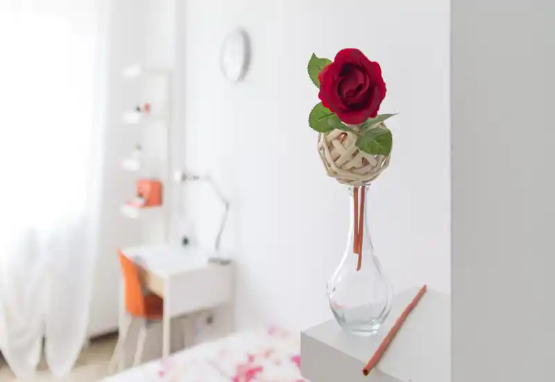 Angolo camera luminoso e ben curato con un vaso decorativo in primo piano e scrivania e letto appena visibili sullo sfondo sfocato.