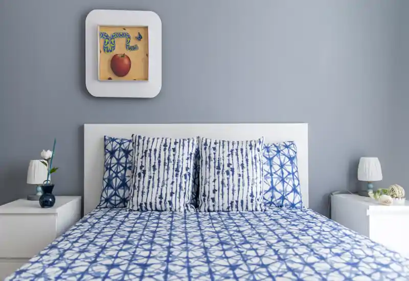 Dormitorio moderno y luminoso con cama doble bien hecha con ropa de cama azul estampada, cabecero blanco y mesitas de noche a juego con lámparas.