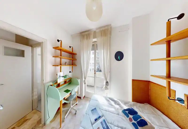 Dormitorio compacto y luminoso con cama confortable, estanterías de madera y un pequeño escritorio verde menta junto a la ventana que da a un balcón.