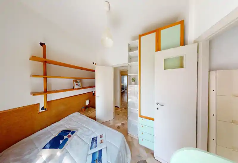 Dormitorio compacto y luminoso con cama bien hecha, estanterías y armario empotrado — ideal para un alquiler acogedor de estilo moderno.