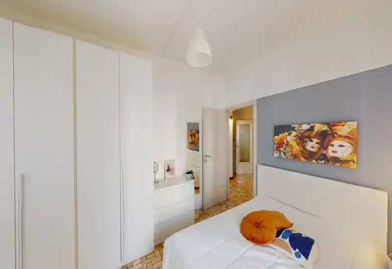 Dormitorio luminoso y bien presentado con cabecero blanco, cojines decorativos y cuadro colorido. Armario empotrado y cómoda ofrecen buen almacenamiento y un ambiente ordenado y acogedor.
