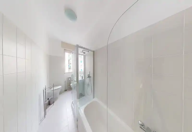 Bright, modern bathroom with a bathtub and an enclosed shower cubicle, white tiles and a window providing natural light.
