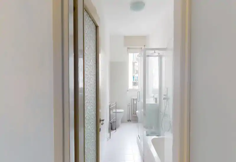 Bright, compact bathroom with a walk-in shower cabin, bathtub edge, toilet and a small window providing natural light.