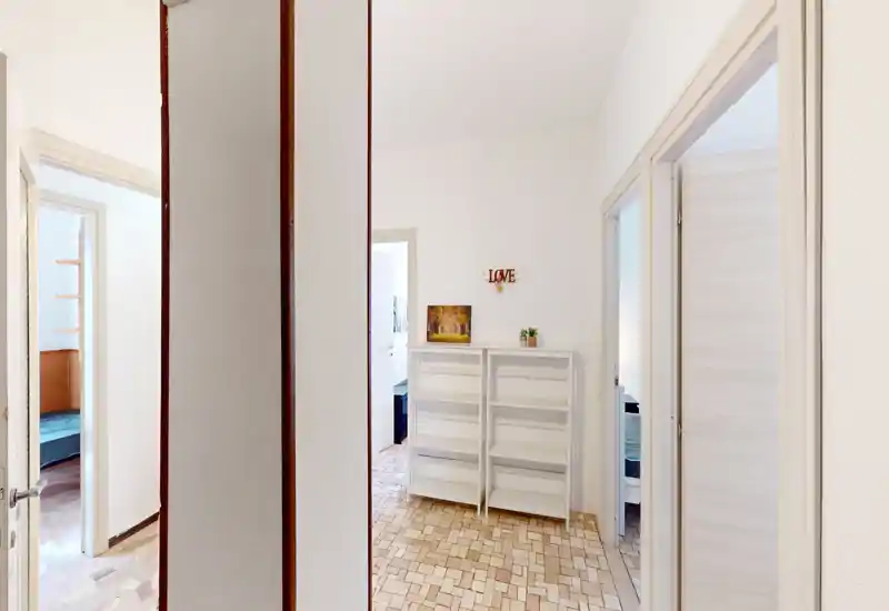 Bright, neutral entrance hallway with tiled floor, a small shelving unit and multiple doorways leading to adjacent rooms — clean and welcoming first impression.