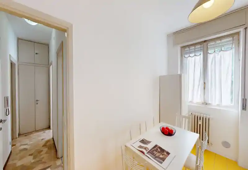 Compact, bright dining nook with a white table, four wire chairs and a large window that provides natural light; styled with a bowl of fruit and an open magazine for a welcoming touch.