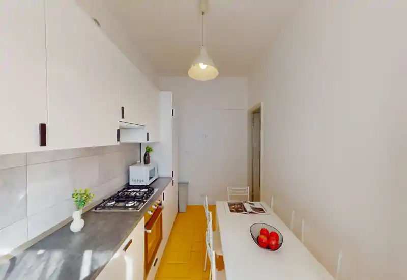 Bright, modern galley kitchen with white cabinets, gas hob, countertop appliances and a small dining table — clean and well lit for comfortable meal preparation.