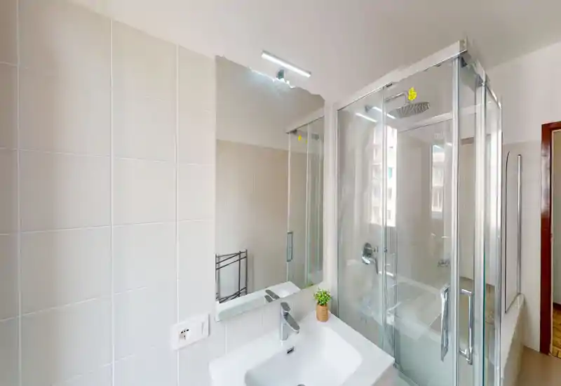 Clean, modern bathroom with a corner glass shower, white sink and a large mirror reflecting light — bright and functional space ideal for short-term rentals.
