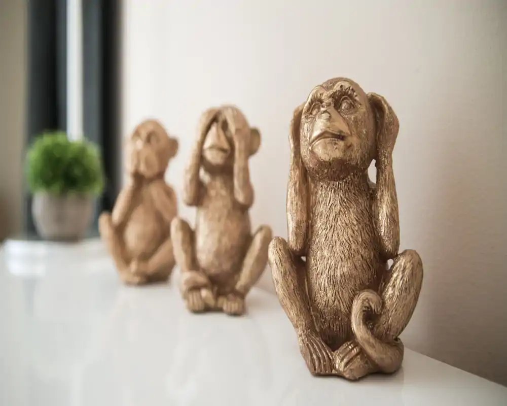 Decorative close-up of three golden monkey statues on a glossy surface with a small potted plant blurred in the background. This image highlights styling and decor details suitable for listing accents or amenities.
