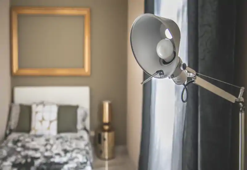 Stylish bedroom shot with a visible bed, decorative cushions and warm, tasteful decor; a modern floor lamp in the foreground adds character and soft natural light.