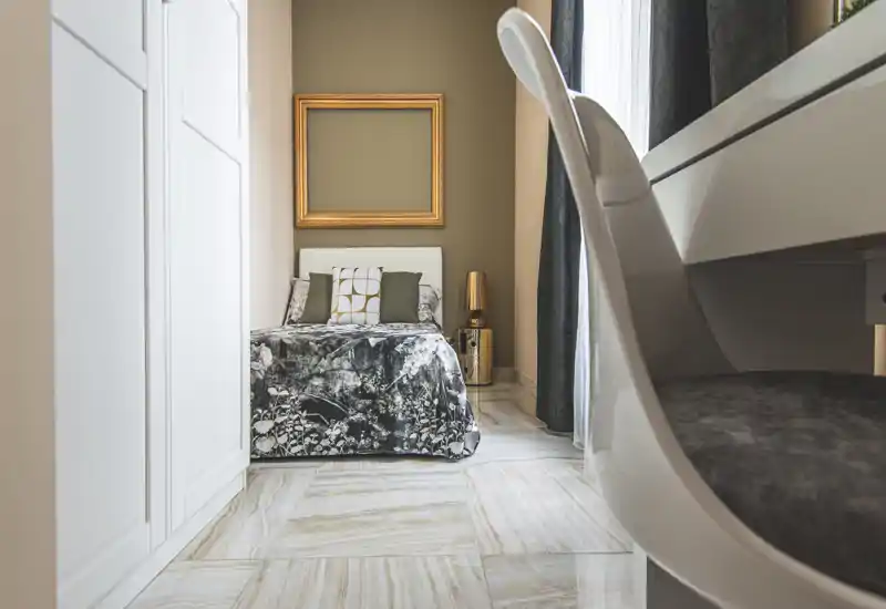 Compact, stylish bedroom with a patterned bedspread, decorative cushions and a bedside lamp. Bright natural light and tasteful neutral tones create a cozy, modern atmosphere.