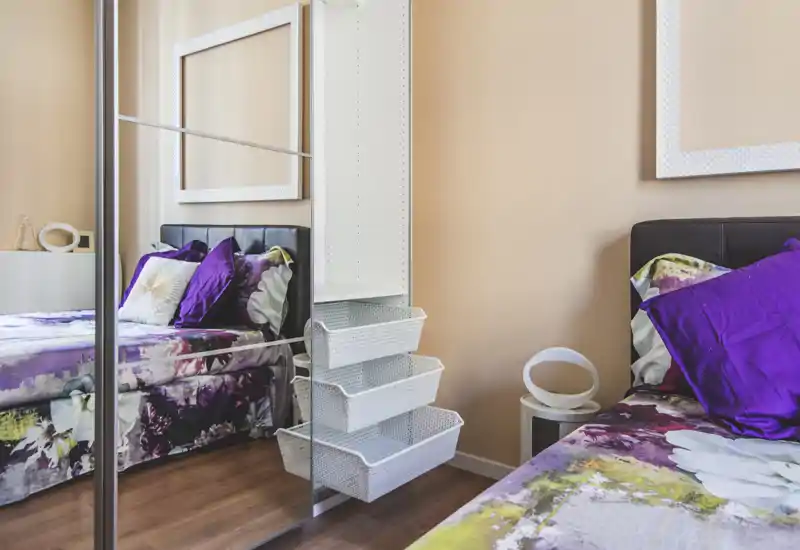 Bright, stylish bedroom with patterned bedding, purple accent pillows and a mirrored wardrobe reflecting the bed for a sense of space.