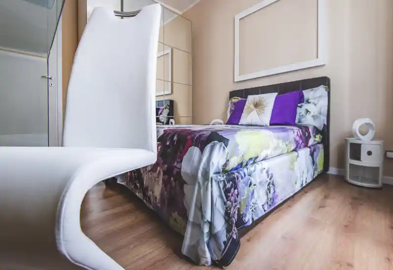 A stylish, well-lit bedroom with a floral-patterned bed, decorative pillows and a modern bedside table. The composition highlights the mattress and textiles for a cozy rental listing.