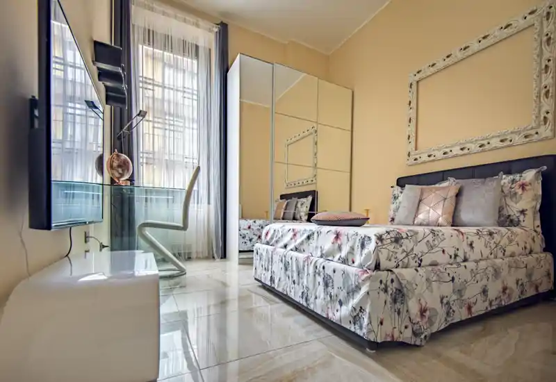 Bright, stylish bedroom with floral bedding, a mirrored wardrobe and a desk by the window offering natural light — comfortable and well-styled for rental photos.