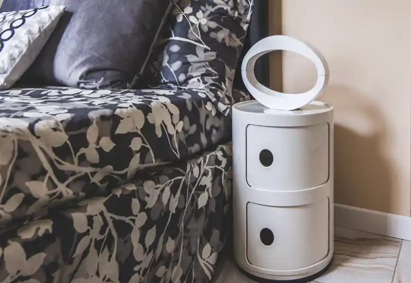 Cozy bedroom corner with patterned bedding, cushions and a modern round bedside unit; soft, well-lit styling ideal for rental photos.