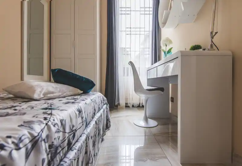 Bright, well-styled bedroom with patterned bedding, decorative cushions and a white dressing desk by the window — ideal for a cozy single or guest room.