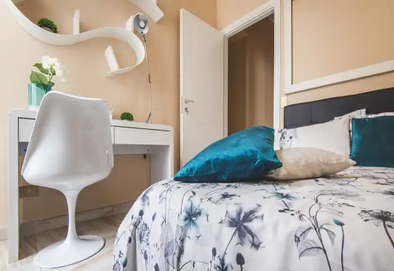 Bright, styled bedroom with a patterned duvet, decorative cushions and a small desk — ideal for a cozy single or double room.