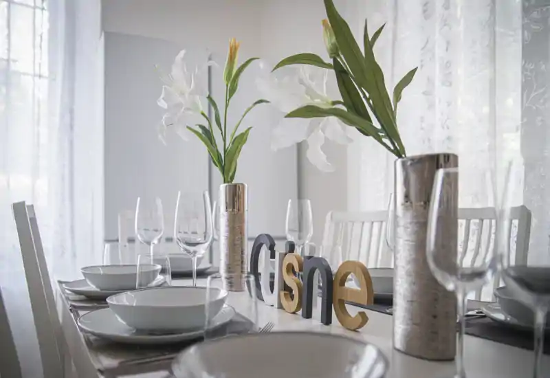 Elegantly set dining table with white crockery, glassware and floral centerpieces in a bright, softly lit room—ideal for showcasing a dining area.