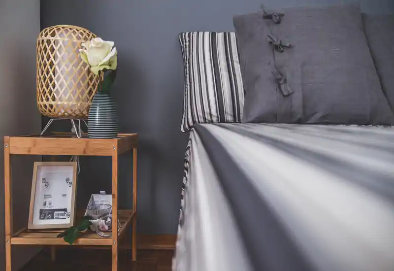 Primo piano di una camera da letto elegante con letto ben rifatto in lenzuola a righe, cuscini coordinati e un comodino in legno con lampada e vaso decorativo.