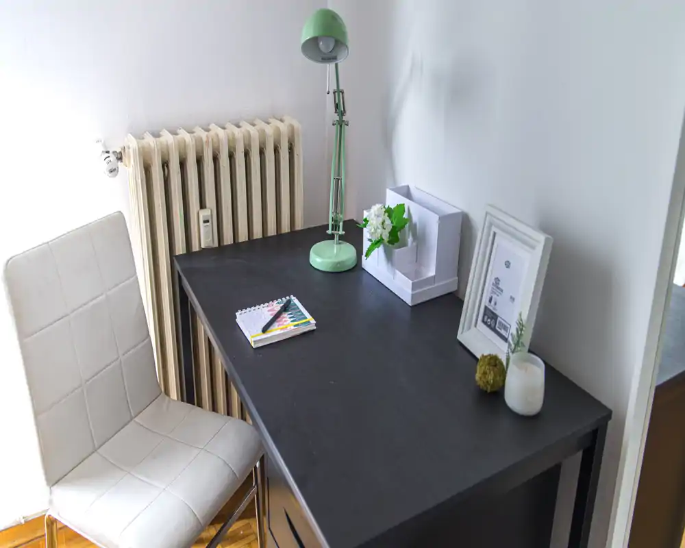 Spazio di lavoro luminoso e ordinato con scrivania nera, lampada verde, cornice decorativa e sedia imbottita confortevole — ideale per lavorare o studiare.
