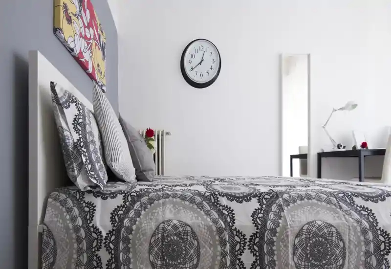 Bright, modern bedroom with a patterned duvet, layered pillows and simple desk in the background — well-staged for rental photos.