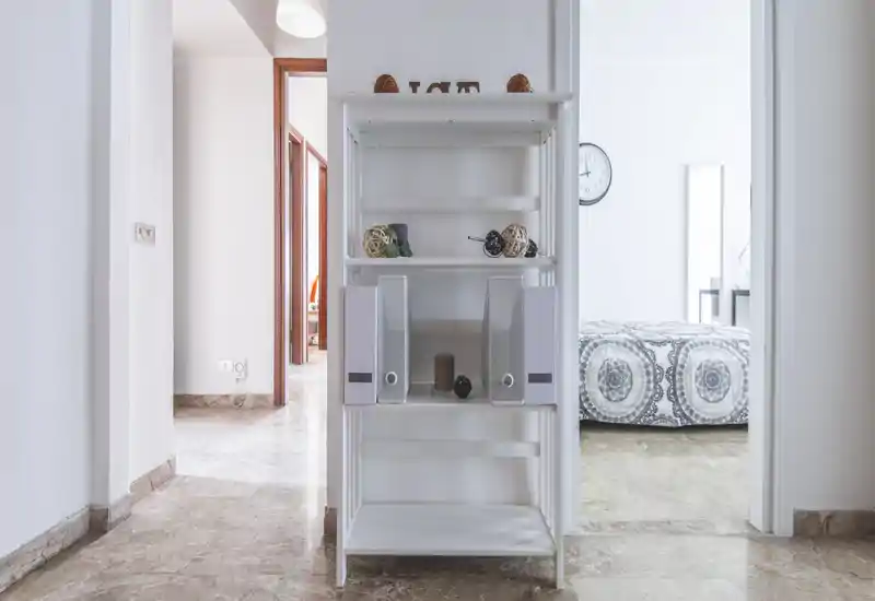Chambre lumineuse et minimaliste vue à travers l'encadrement, avec une couette à motifs et une décoration neutre. La composition met en valeur la zone lit et le couloir attenant pour un rendu propre et aéré.