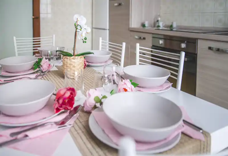 Table à manger lumineuse et dressée pour quatre avec linge pastel et accents floraux, à côté d'une cuisine moderne.