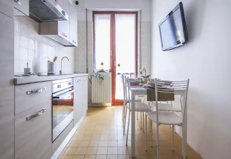 Cuisine lumineuse et compacte avec meubles modernes, four encastré et petite table à manger près d'une porte ensoleillée — idéale pour un appartement convivial.