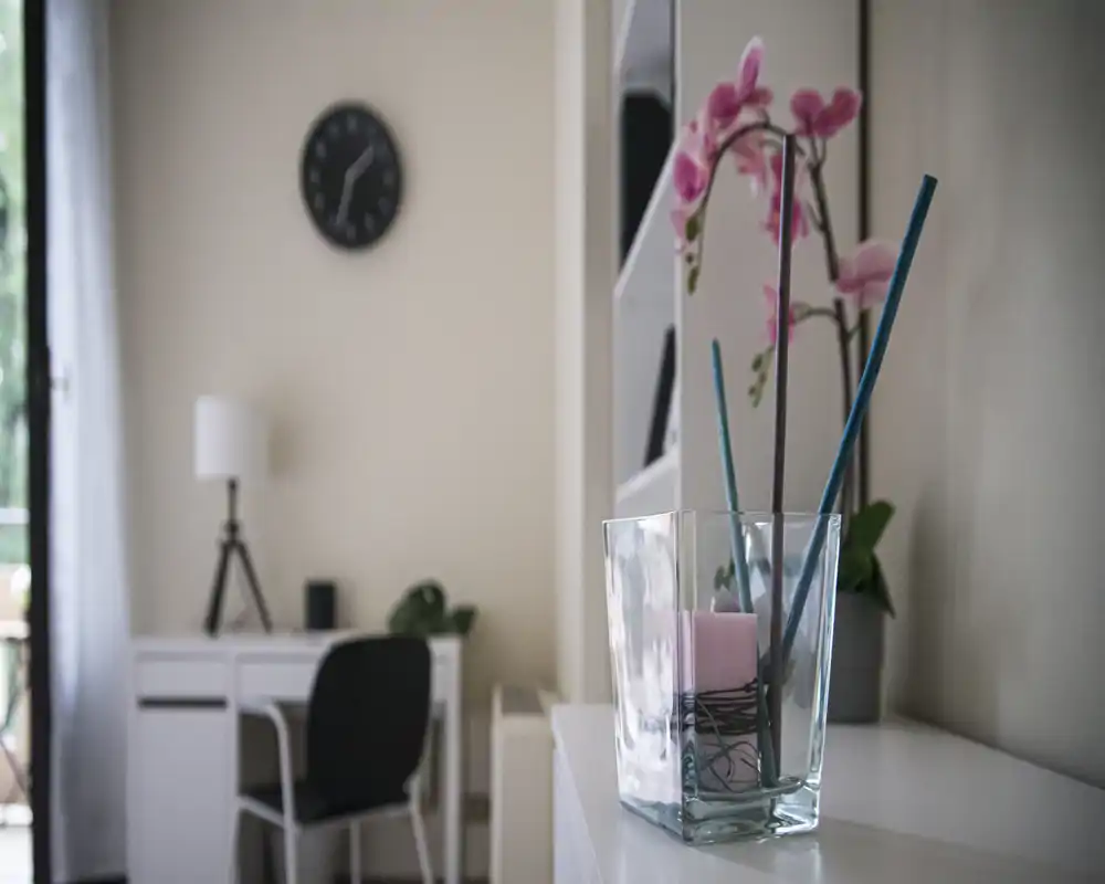 Zona giorno accogliente e ben illuminata con una scrivania elegante e un'orchidea decorativa in primo piano; la luce naturale e gli elementi di stile rendono l'ambiente invitante.