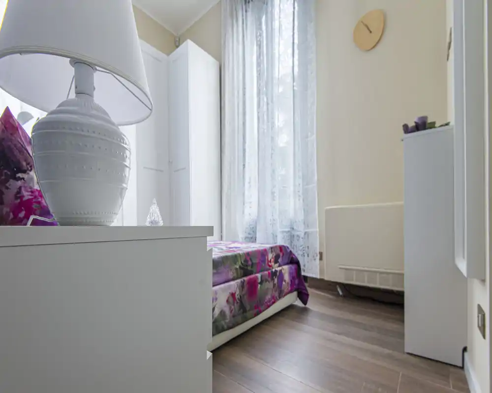 Bright, cozy bedroom with a floral bedspread, white furniture and a large window letting in natural light — ideal for a comfortable stay.