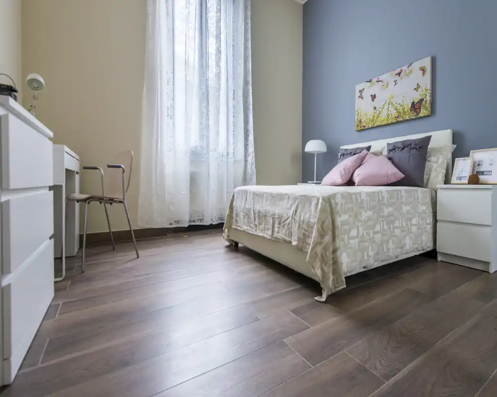Camera da letto luminosa e ben arredata con un comodo letto matrimoniale, cuscini morbidi e una bella decorazione a parete; la luce naturale attraverso la tenda crea un'atmosfera accogliente.