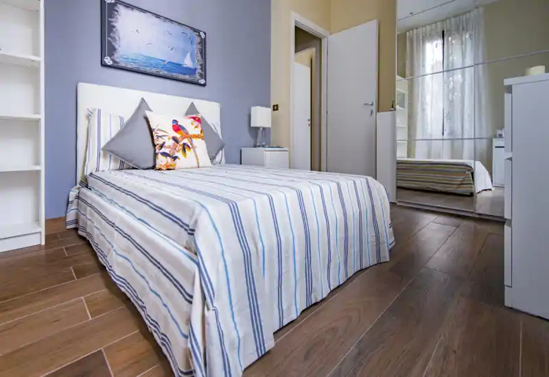 Camera da letto luminosa e ben allestita con letto matrimoniale dalle lenzuola rigate, cuscini decorativi e testiera elegante; armadio con specchio che amplia lo spazio.