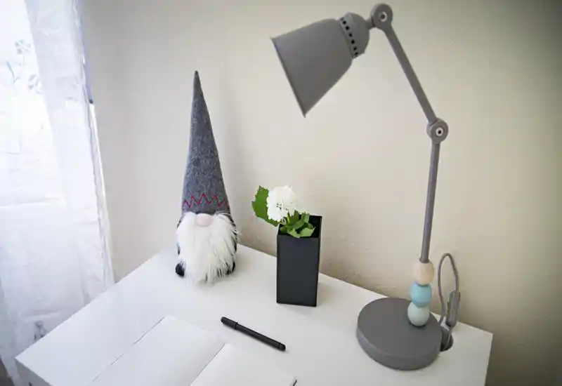 Bright, minimal bedside or desk vignette with a modern adjustable lamp, small plant and decorative gnome — a cozy, well-lit corner ideal for reading or work.